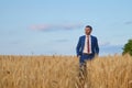 Young farmer businessman in shirt and tie inspects his fields with crops
