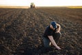 Farmer examing dirt while tractor is plowing field Royalty Free Stock Photo