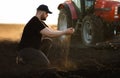 Farmer examing dirt while tractor is plowing field Royalty Free Stock Photo