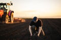 Farmer examing dirt while tractor is plowing field Royalty Free Stock Photo