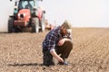 Young farmer examing dirt while tractor is plowing field Royalty Free Stock Photo