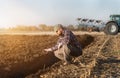 Young farmer examing planted wheat while tractor is plowing fie