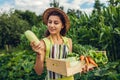 Young farmer holding zucchini and wooden box filled with fresh vegetables. Woman gathered autumn crop. Gardening