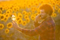 Young farmer standing in the middle of a golden sunflower field smiling and talking on phone while holding up a sunflower oil Royalty Free Stock Photo