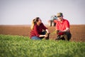 Young farmers examing planted wheat while tractor is plowing fi