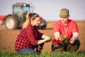 Young farmers examing planted wheat while tractor is plowing fi Royalty Free Stock Photo