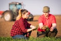 Young farmers examing planted wheat while tractor is plowing fi