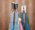 Young fashion couple's legs in jeans and sneakers feet up and holding hands on the wall. Close up. Warm color. Indoor.