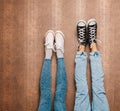 Young fashion couple's legs in jeans and sneakers feet up on the wall. Close up. Indoor. Warm color