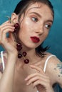 Young fashion freckled model with cherry berries in front of blue background