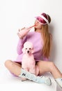 Young fashion glamour woman in winter long dress and cap holding pink poodle dog and drinking from bottle