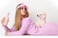 Young fashion glamour woman in winter long dress and cap holding pink poodle dog and drinking from bottle