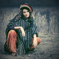 Young fashion hipster woman in rasta poncho sitting on the ground Royalty Free Stock Photo