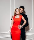 Young fashion man and woman against white wall, looking at the camera. He hugs her from behind. Indoor. Warm color. Royalty Free Stock Photo