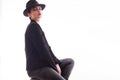 Young fashion model with a stylish hat and jacket posing sitting on a char in studio over white background Royalty Free Stock Photo