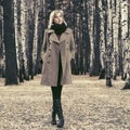 Young fashion woman in classic beige coat walking in autumn forest Royalty Free Stock Photo