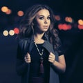 Young fashion woman in long sleeveless coat walking on city street at night