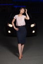 Young fashion woman next to her car on city street at night