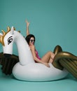 Young fashion woman relaxing with big inflatable unicorn pegasus float mattress in sexy pink bikini for swimming pool Royalty Free Stock Photo