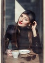 Young fashion woman sitting in cafe on the street with cup of cappuccino. Outdoors portrait in retro style Royalty Free Stock Photo