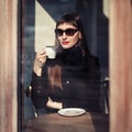 Young fashion woman sitting in cafe on the street with cup of cappuccino. Outdoors portrait in retro style