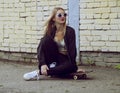 Young fashion woman sitting on skateboard. Girl in sunglasses with longboard on city streets Royalty Free Stock Photo