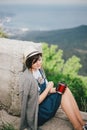 Young fashion woman sitting on a top of the mountain drinking tea with beautiful mountains and ocean view on the background Royalty Free Stock Photo