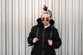 Young fashionable beautiful hipster woman with a stylish hairstyle with a bandana in black sunglasses in a long black coat with a Royalty Free Stock Photo