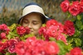 Young fashionable girl in a blue hat stands among the red roses. Stylish woman with closed eyes sniffs pink flowers Royalty Free Stock Photo