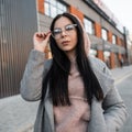 Young fashionable hipster woman straightens stylish glasses outdoors. Portrait pretty beautiful girl in stylish pink hoodie in Royalty Free Stock Photo
