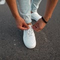 Young fashionable manstraightens laces on trendy white leather sneakers. New stylish collection of men`s shoes. Summer fashion. Royalty Free Stock Photo