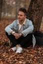 Young fashionable nice man with a stylish hairstyle with beard  in trendy clothing is resting outdoors in a park sitting on orange Royalty Free Stock Photo