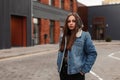 Young fashionable pretty urban woman in youth blue denim jacket is poses near building in the city. American beautiful girl in Royalty Free Stock Photo