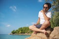 Young fashionable stylish handsome latin man in a white t-shirt and sunglasses on a bright tropical beach, vacation and travel to Royalty Free Stock Photo