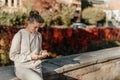 Young Fashionable Teenage Girl With Smartphone In Europian Park In Autumn Sitting At Smiling. Trendy Young Woman In Fall Royalty Free Stock Photo