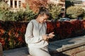 Young Fashionable Teenage Girl With Smartphone In Europian Park In Autumn Sitting At Smiling. Trendy Young Woman In Fall Royalty Free Stock Photo