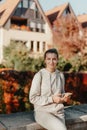 Young Fashionable Teenage Girl With Smartphone In Europian Park In Autumn Sitting At Smiling. Trendy Young Woman In Fall Royalty Free Stock Photo