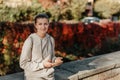 Young Fashionable Teenage Girl With Smartphone In Europian Park In Autumn Sitting At Smiling. Trendy Young Woman In Fall Royalty Free Stock Photo