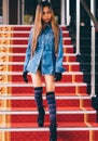 Young fashionable woman in blue jeans, and long striped knee socks walking down on stairs with the red carpet Royalty Free Stock Photo