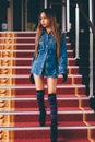Young fashionable woman in blue jeans, and long striped knee socks walking down on stairs with the red carpet Royalty Free Stock Photo
