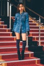 Young fashionable woman in blue jeans, and long striped knee socks walking down on stairs with the red carpet