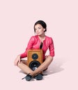 Young fashionable woman in a pink jacket sits on the floor clutching a wooden speaker