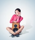 Young fashionable woman in a pink jacket sits on the floor clutching a wooden speaker