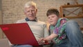 Young fat boy teaches grandpa how to use a laptop. Difference of generations. Home comfort, family idyll, cosiness