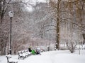 Young father with baby carriage sit on a bench covered with snow in a city park in winter season
