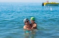 Young father in black sunglasses and smiling baby boy son in green baseball cap playing in the sea in the day time. Positive human Royalty Free Stock Photo