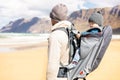 Young father carrying his infant baby boy son in backpack on windy sandy beach. Family travel and winter vacation