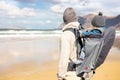 Young father carrying his infant baby boy sun in backpack on windy sandy beach of Famara, Lanzarote island, Spain