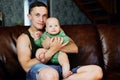 Young father of European appearance holds his 6 month old daughter in his arms while sitting on sofa in living room. Royalty Free Stock Photo