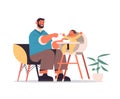 young father feeding his little son on kids eating chair fatherhood concept dad spending time with his kid Royalty Free Stock Photo